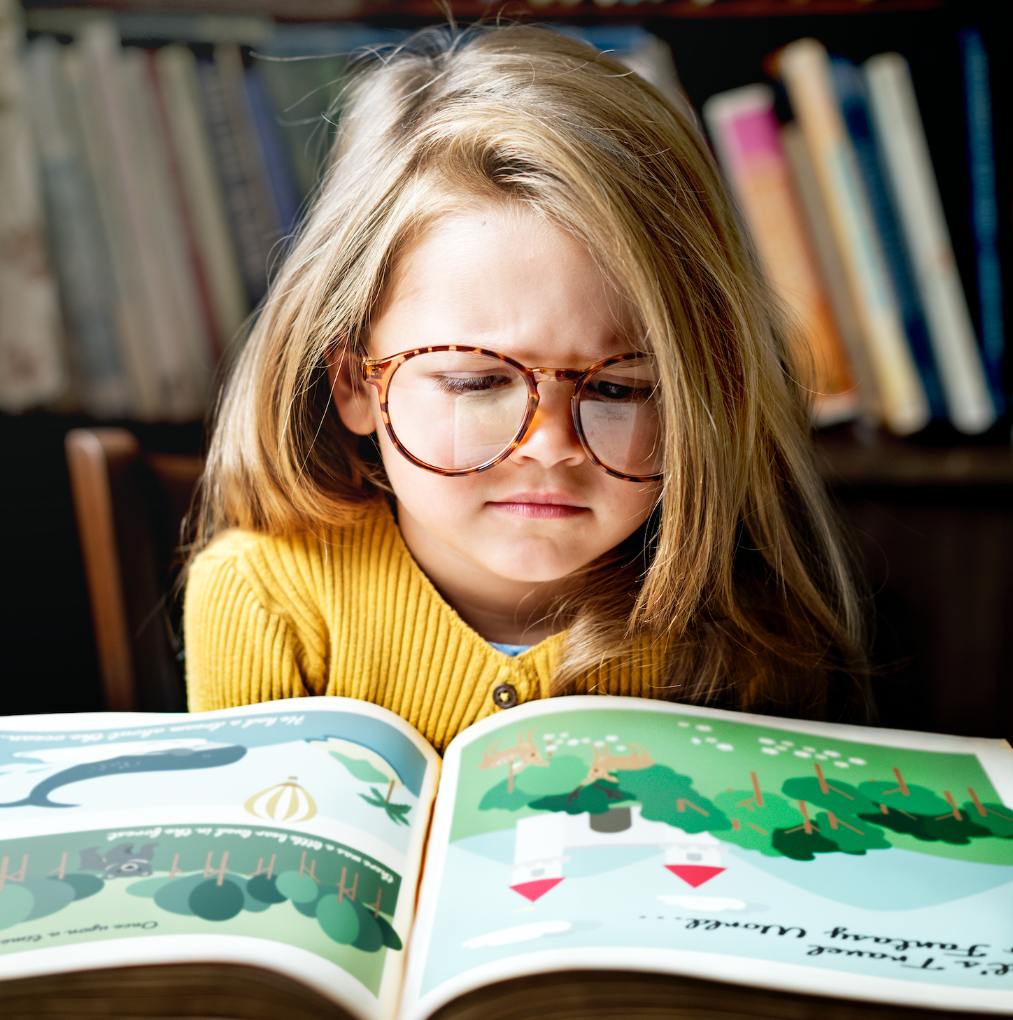 Niña usando anteojos redondos de carey leyendo un libro infantil en biblioteca